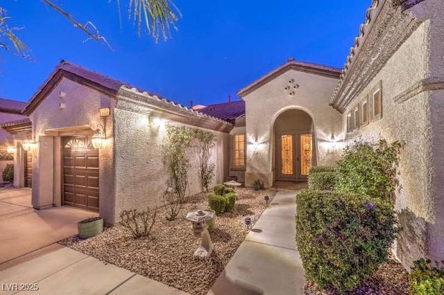 doorway to property with an attached garage, stucco siding, a tiled roof, and french doors