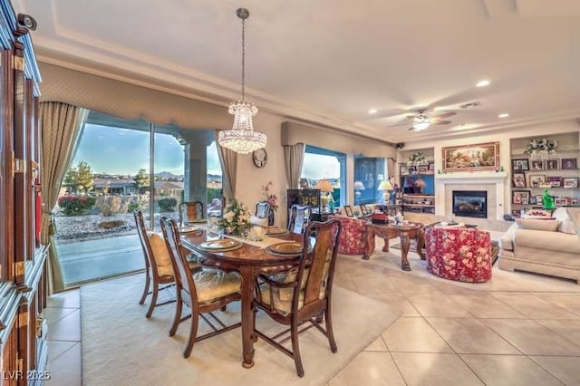 dining space featuring light tile patterned floors, a glass covered fireplace, a ceiling fan, and a healthy amount of sunlight