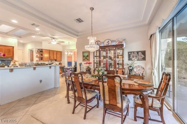 dining space with light tile patterned floors, a tray ceiling, ceiling fan with notable chandelier, and visible vents