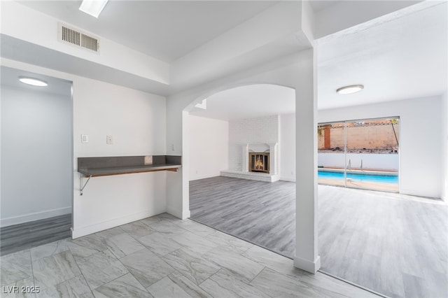 unfurnished living room featuring a brick fireplace, baseboards, visible vents, and marble finish floor