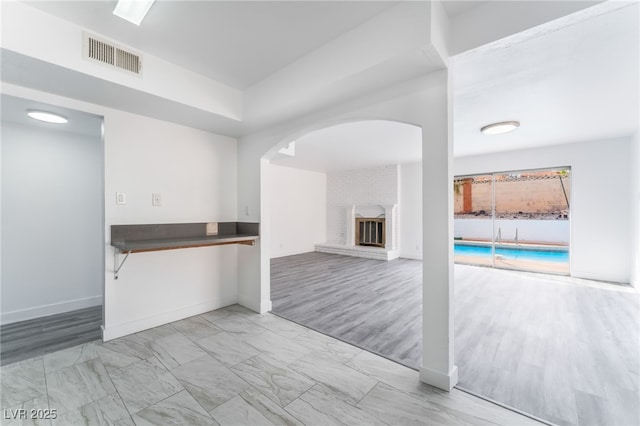 unfurnished living room with light wood-type flooring, baseboards, visible vents, and arched walkways