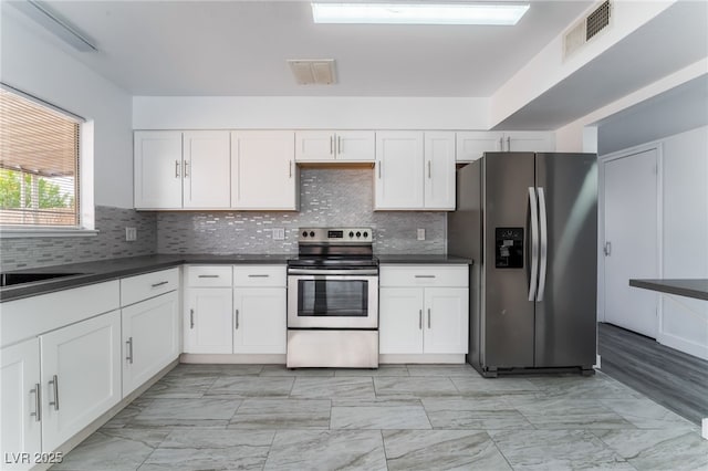 kitchen with visible vents, white cabinets, dark countertops, stainless steel appliances, and backsplash