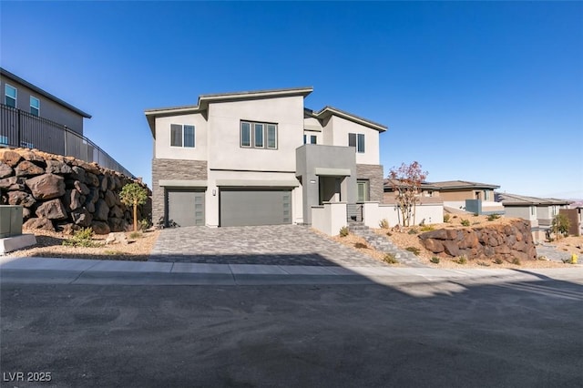 modern home featuring an attached garage, stone siding, decorative driveway, a residential view, and stucco siding