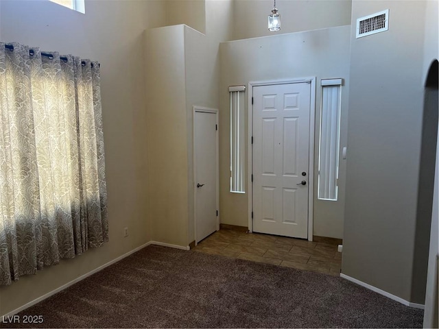 carpeted entryway with baseboards, a high ceiling, and visible vents