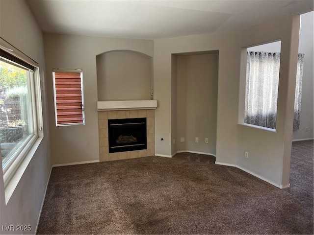 unfurnished living room featuring a fireplace, dark carpet, and baseboards