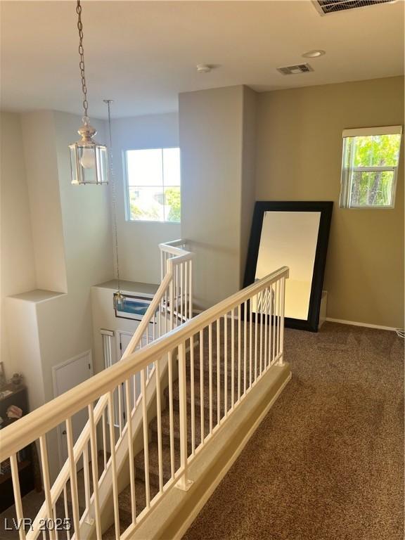 corridor featuring visible vents, dark carpet, an upstairs landing, and a wealth of natural light