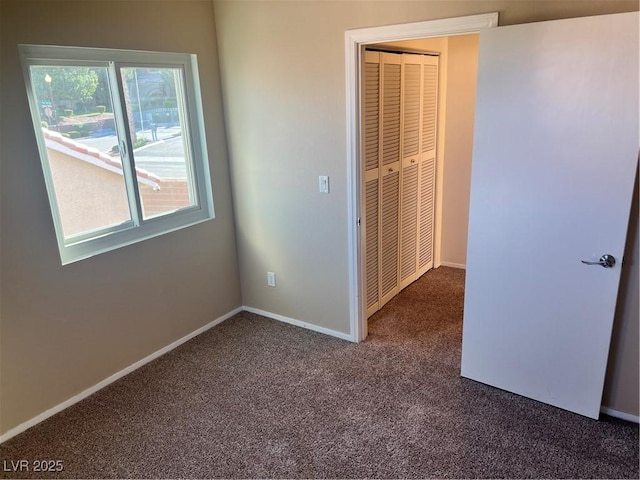 unfurnished bedroom with baseboards, dark carpet, and a closet