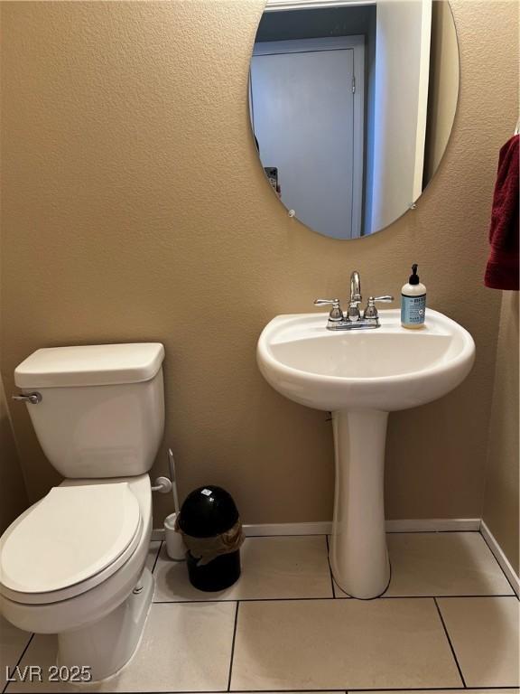 bathroom with toilet, baseboards, and tile patterned floors