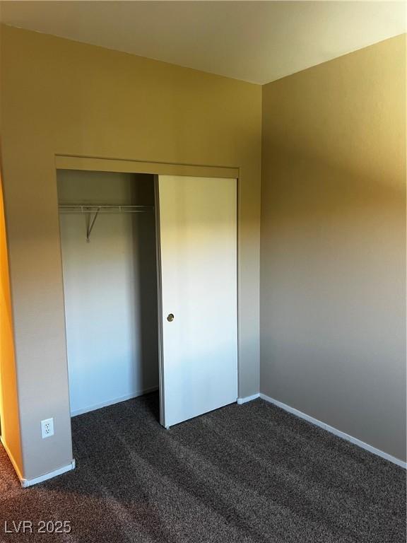 unfurnished bedroom featuring baseboards, dark carpet, and a closet