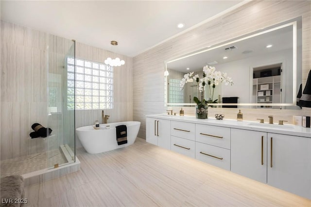 bathroom with double vanity, a stall shower, a freestanding tub, tile walls, and a sink