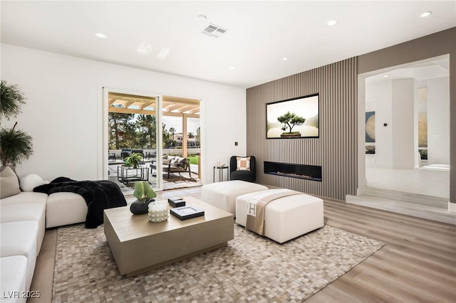 living room with wood finished floors, visible vents, a fireplace, recessed lighting, and an accent wall