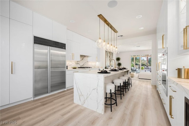 kitchen featuring stainless steel built in refrigerator, decorative backsplash, white cabinets, and light wood-style floors