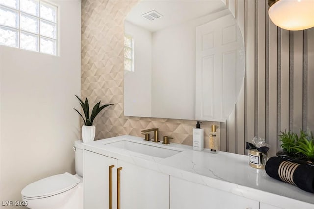 half bath with a wealth of natural light, visible vents, toilet, and vanity