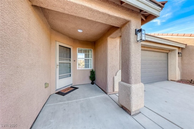 property entrance featuring a garage, driveway, and stucco siding