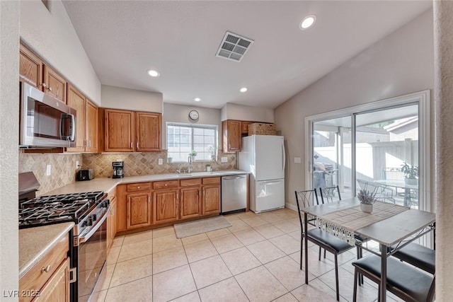 kitchen with brown cabinets, stainless steel appliances, light countertops, visible vents, and decorative backsplash