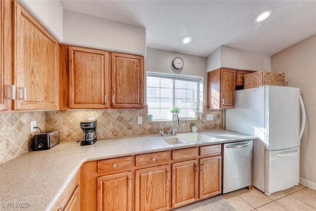 kitchen with light countertops, backsplash, freestanding refrigerator, a sink, and dishwasher