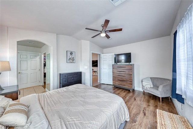 bedroom featuring arched walkways, lofted ceiling, visible vents, light wood-style floors, and baseboards