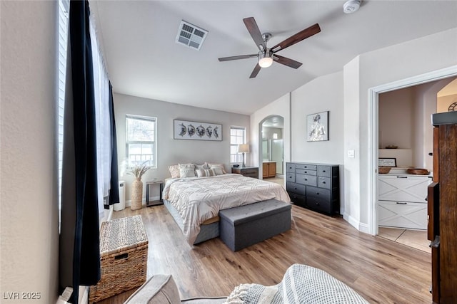 bedroom with light wood-style floors, arched walkways, visible vents, and vaulted ceiling