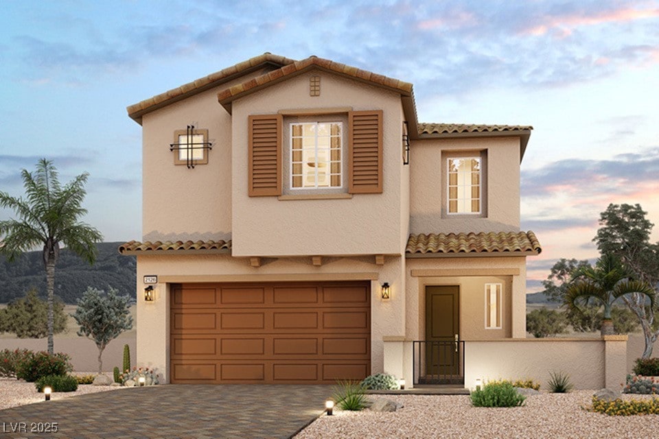 mediterranean / spanish-style home featuring decorative driveway, an attached garage, a tile roof, and stucco siding