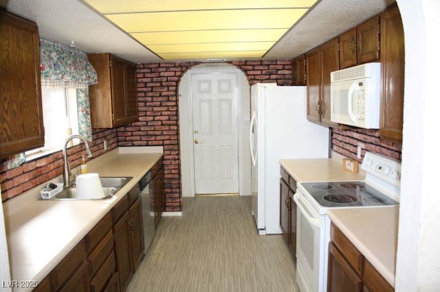 kitchen featuring light countertops, a sink, brick wall, light wood-type flooring, and white appliances