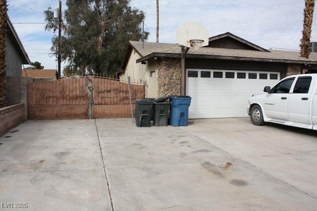 view of side of home with a garage, concrete driveway, fence, and stone siding