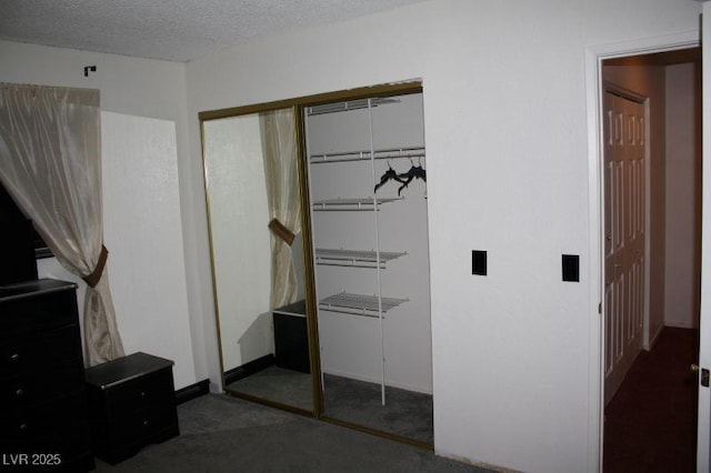 unfurnished bedroom featuring a textured ceiling, dark colored carpet, and a closet