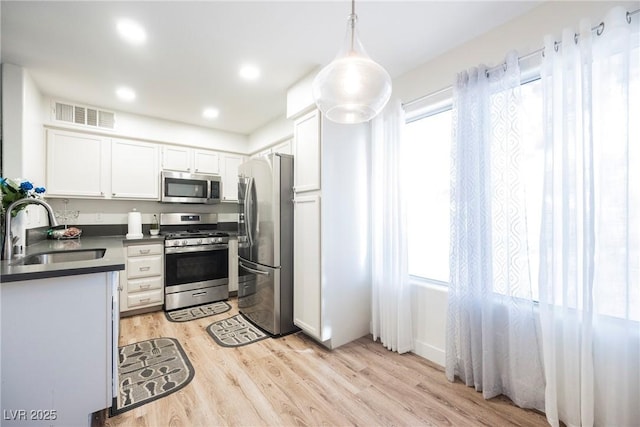 kitchen with visible vents, a sink, dark countertops, light wood-style floors, and appliances with stainless steel finishes