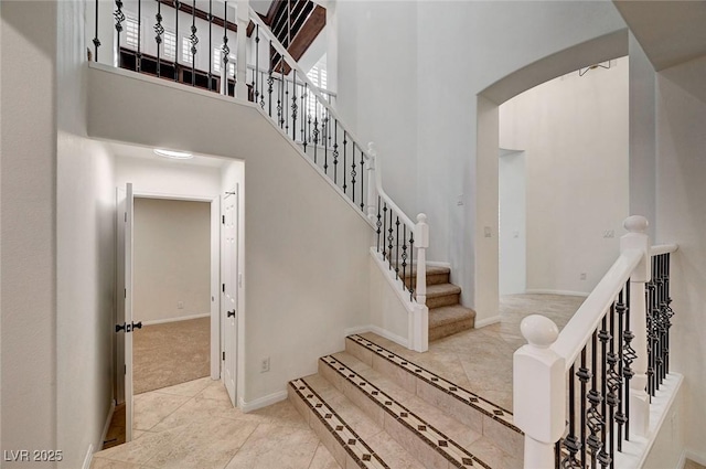 staircase with a towering ceiling, baseboards, and arched walkways