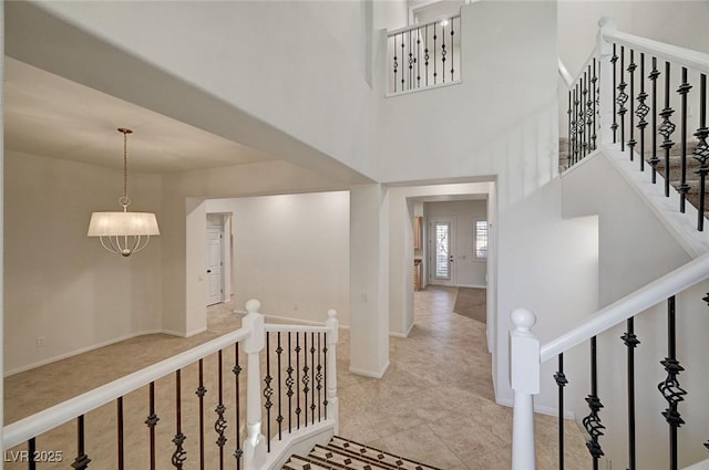 hallway with baseboards, stairs, a towering ceiling, and an inviting chandelier