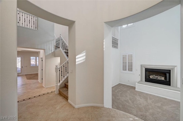 stairs featuring carpet floors, a high ceiling, a glass covered fireplace, and visible vents