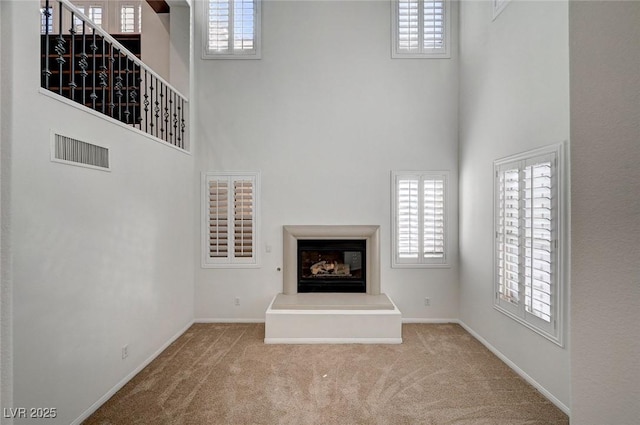 unfurnished living room with visible vents, a high ceiling, a glass covered fireplace, light carpet, and baseboards