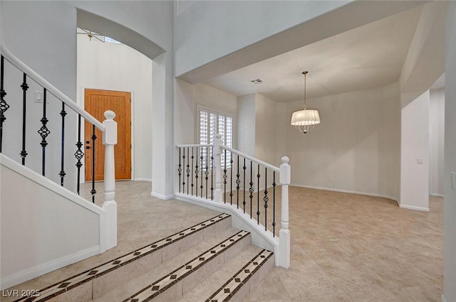 entryway featuring visible vents, baseboards, stairway, an inviting chandelier, and a high ceiling