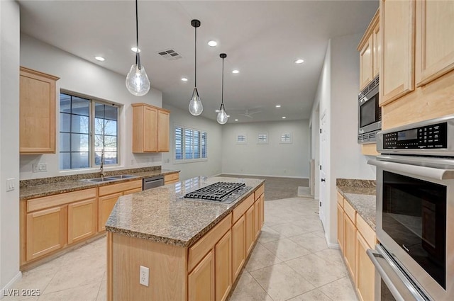 kitchen with light brown cabinets, a sink, a kitchen island, appliances with stainless steel finishes, and decorative light fixtures