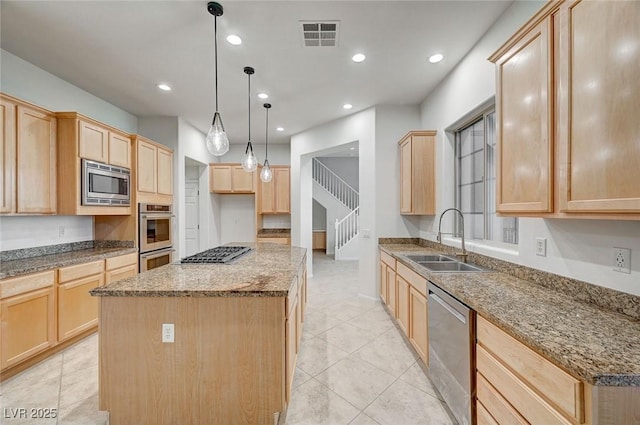 kitchen with light brown cabinets, stainless steel appliances, a sink, a kitchen island, and hanging light fixtures