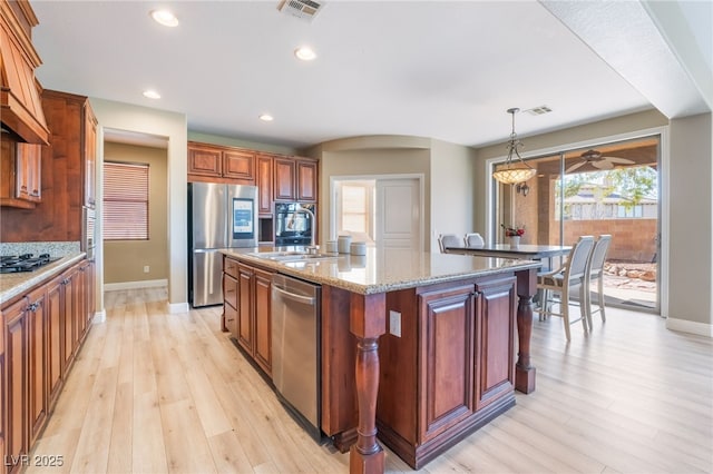 kitchen featuring visible vents, an island with sink, hanging light fixtures, stainless steel appliances, and a sink