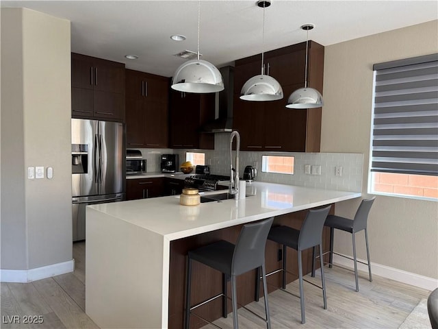 kitchen with extractor fan, a breakfast bar, light countertops, stainless steel fridge with ice dispenser, and pendant lighting