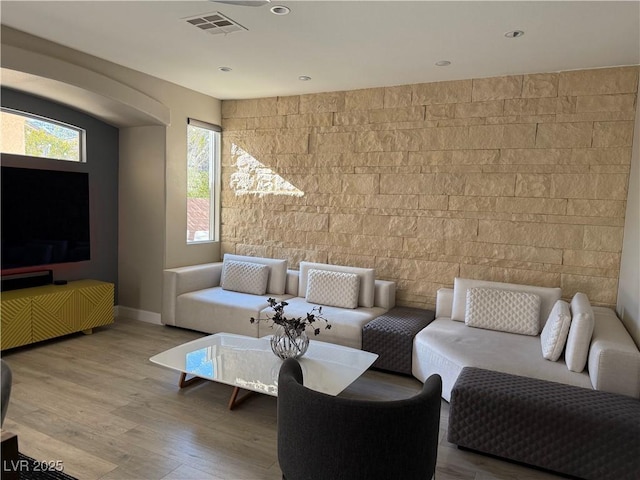 living room featuring an accent wall, visible vents, baseboards, and wood finished floors