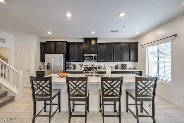 kitchen featuring visible vents, a kitchen breakfast bar, light countertops, appliances with stainless steel finishes, and a center island with sink