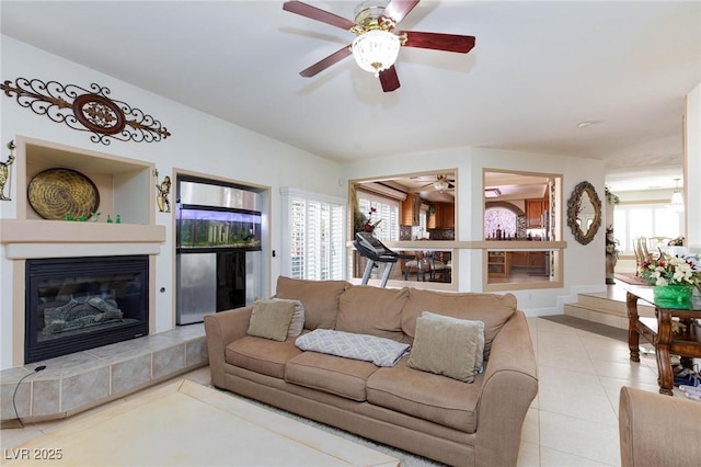 living area with light tile patterned floors, ceiling fan, a tiled fireplace, and a wealth of natural light