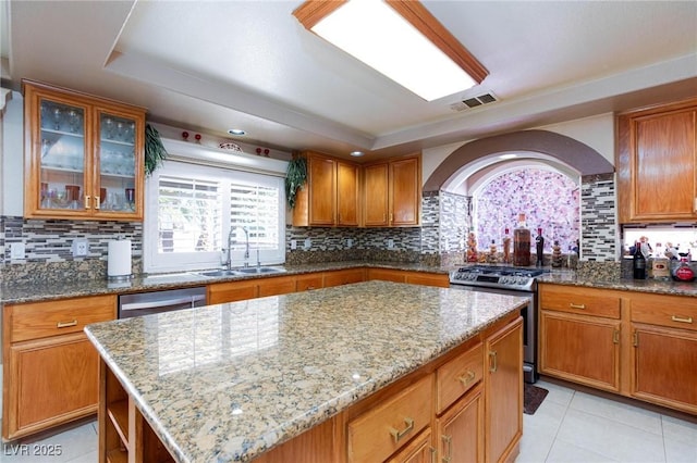 kitchen with brown cabinets, visible vents, appliances with stainless steel finishes, a kitchen island, and a sink