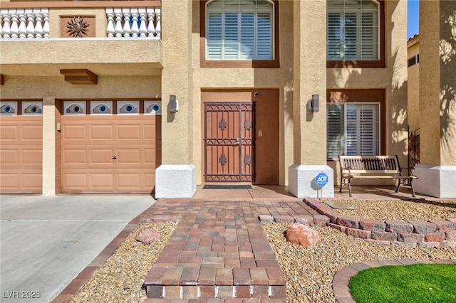 doorway to property featuring driveway, a balcony, an attached garage, and stucco siding