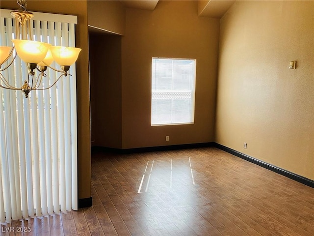 spare room featuring a chandelier, baseboards, and wood finished floors