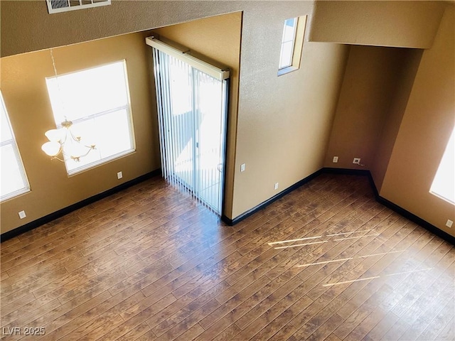 spare room featuring a chandelier, wood-type flooring, visible vents, and baseboards