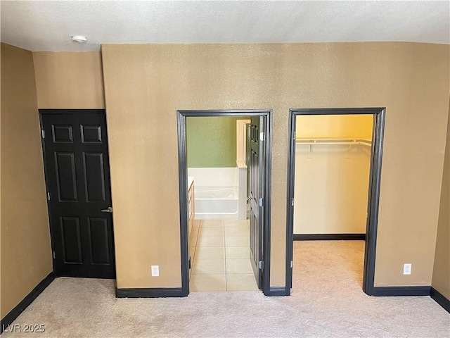 unfurnished bedroom with a closet, light colored carpet, a spacious closet, ensuite bathroom, and baseboards