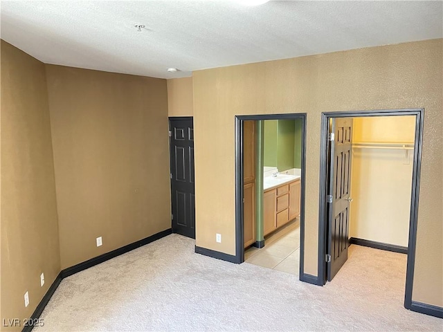 unfurnished bedroom featuring a walk in closet, a closet, light colored carpet, ensuite bath, and baseboards