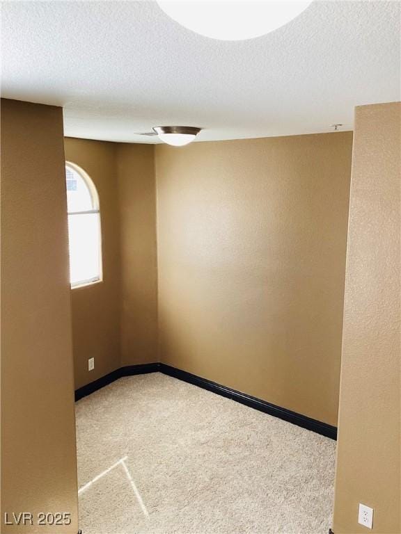 unfurnished room featuring a textured ceiling, carpet, and baseboards