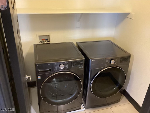 clothes washing area with light tile patterned floors, laundry area, washing machine and clothes dryer, and baseboards