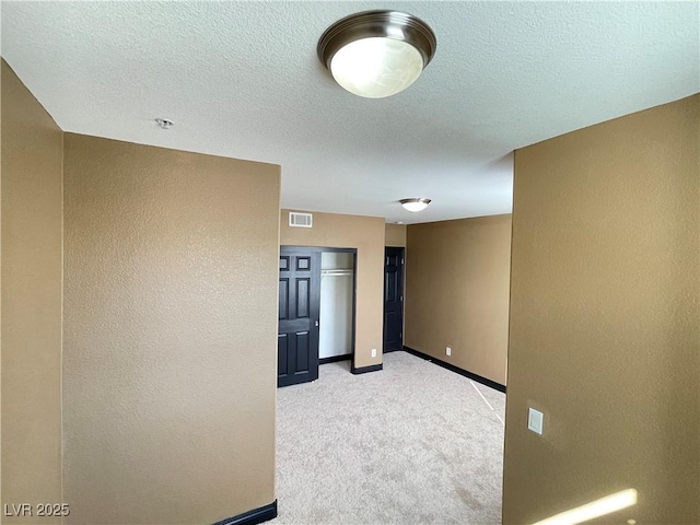 empty room featuring light colored carpet, visible vents, a textured wall, a textured ceiling, and baseboards