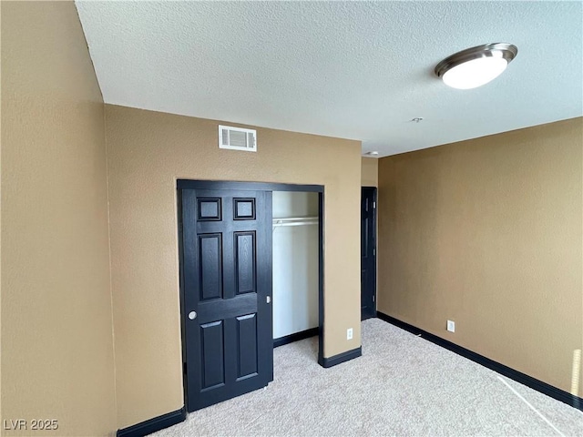 unfurnished bedroom featuring a textured ceiling, light colored carpet, visible vents, baseboards, and a closet