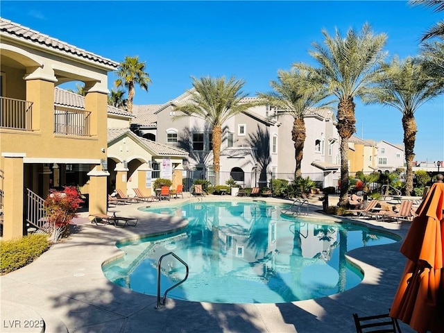 community pool with a patio area, fence, and a residential view